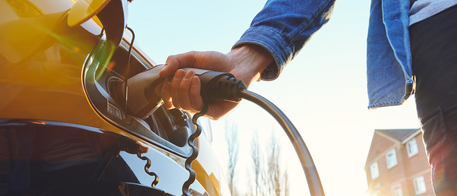 Electric car plugged in outside house on street with a sunset Schlagwort(e): charger, plug-in, phev, mains outlet, rapid charge