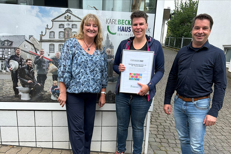 Theresa Becker von Karl Becker Haustechnik mit der Urkunde des Checks Nachhaltigkeit 360° und zwei Handwerkskammerberatern.