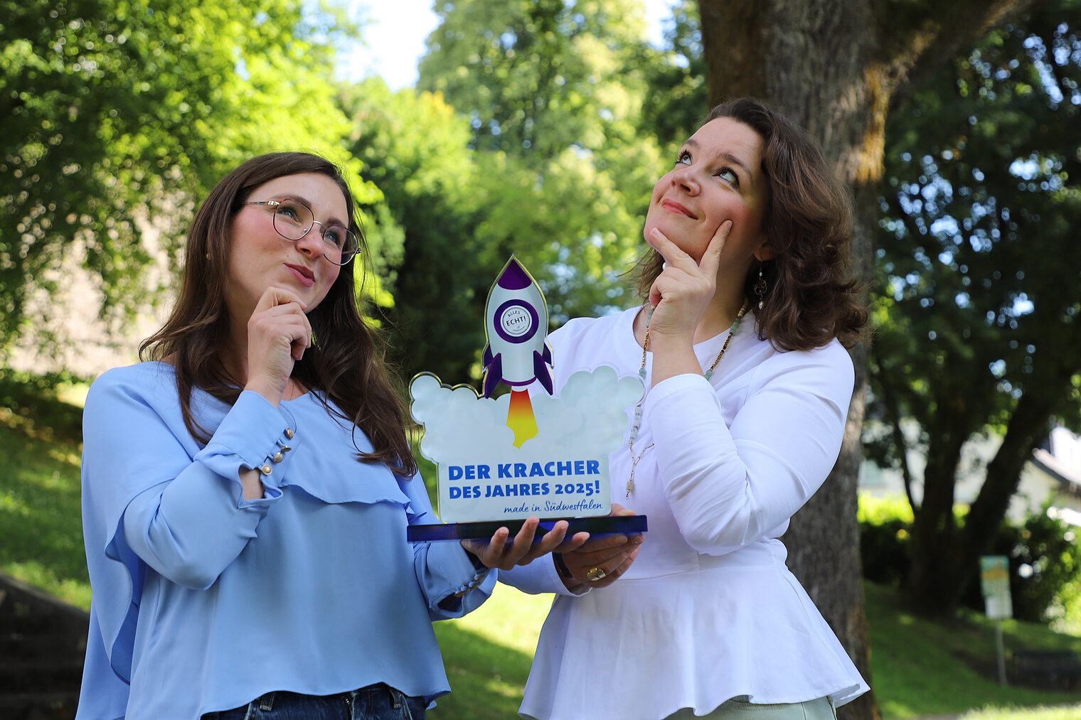 Zwei Frauen halten die Trophäe für den Preis "Kracher des Jahres" in Südwestfalen 2025.
