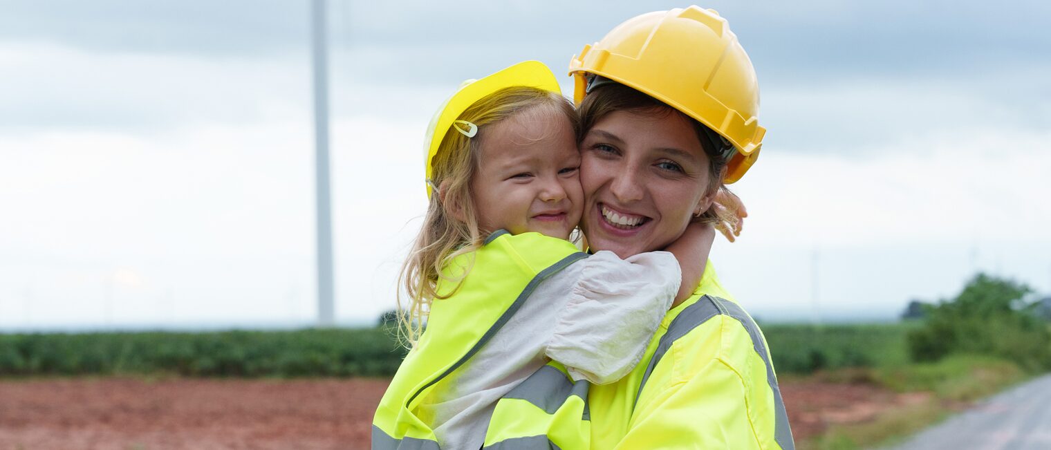 Eine Mutter mit Kind in Warnwesten auf einer Baustelle.