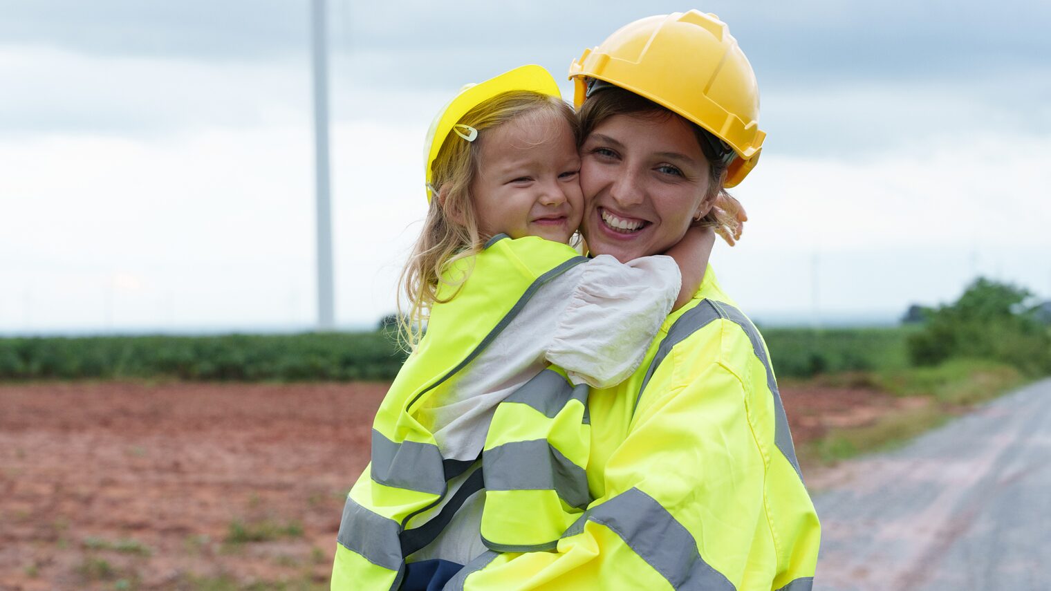 Eine Mutter mit Kind in Warnwesten auf einer Baustelle.