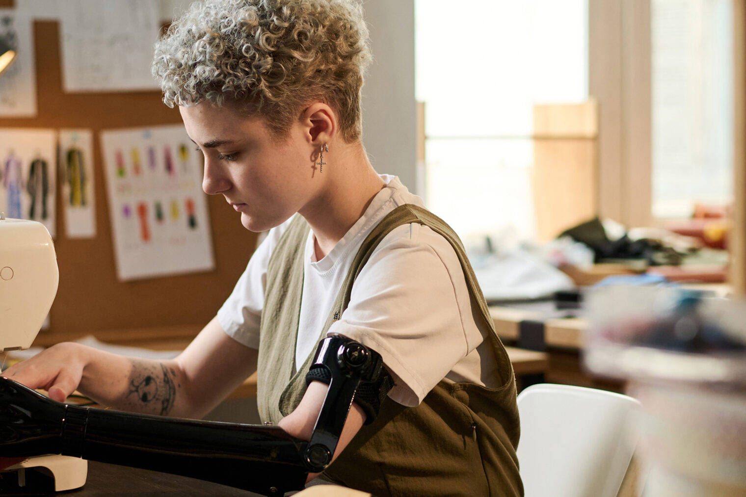 Eine Schneiderin mit Armprothese näht ein Kleidungsstück mit einer Nähmaschine.