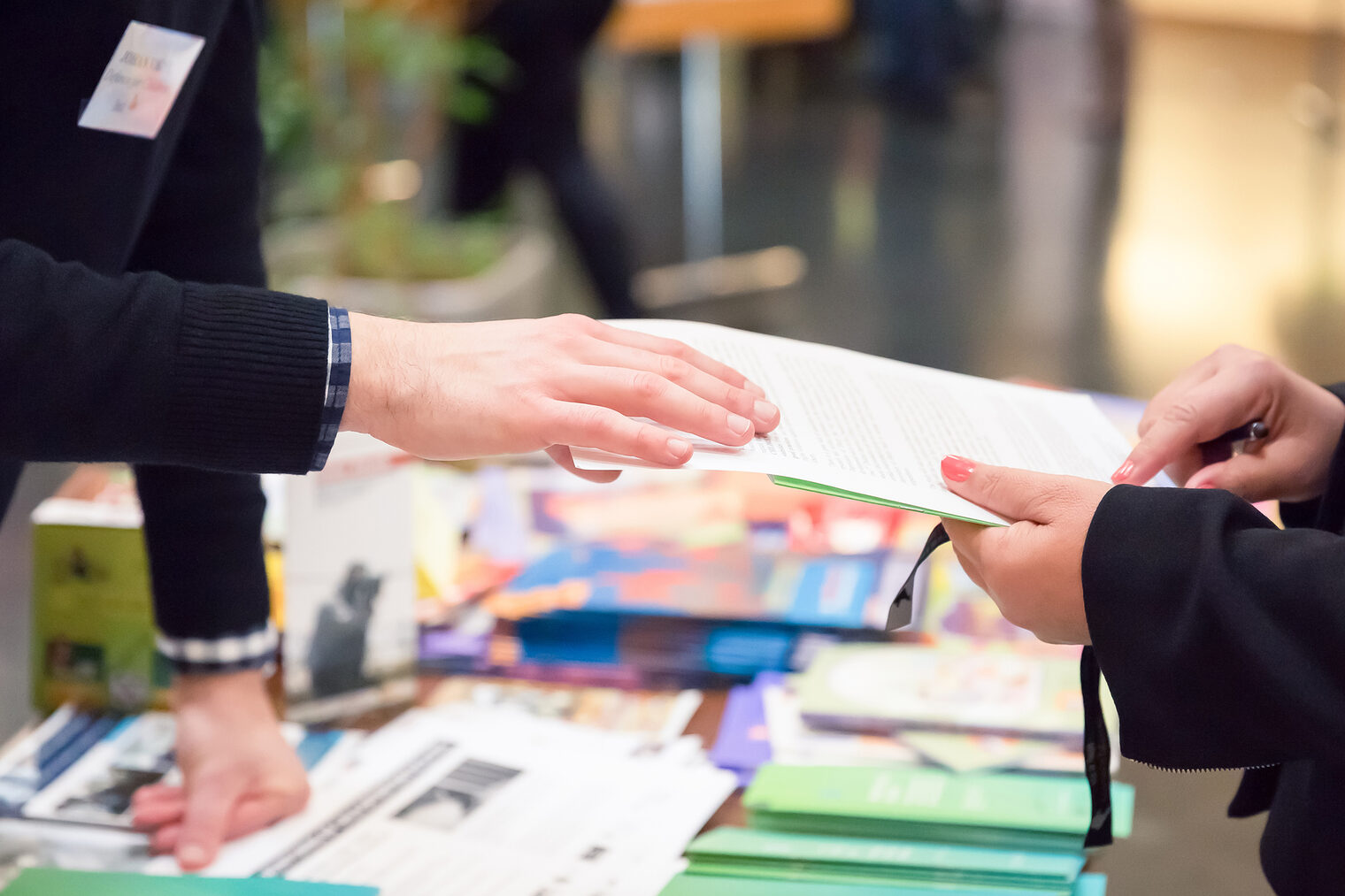Ein Mann reicht einer Frau ein Informationsblatt auf einer Fachmesse.