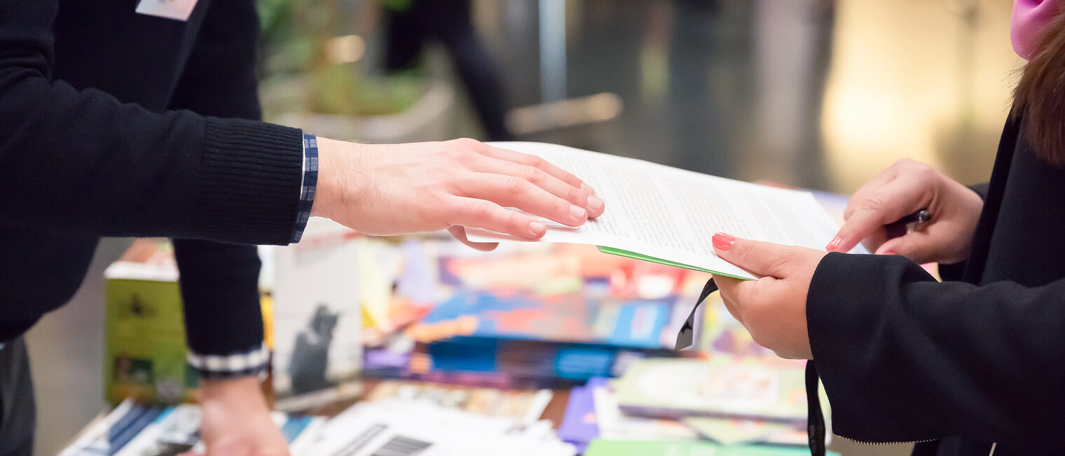 Fachmesse Ein Mann reicht einer Frau ein Informationsblatt auf einer Fachmesse.