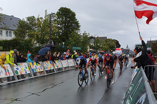 Radrennfahrer sprinten beim Radrennen "Deutschland Tour" auf das Ziel zu. Viele Zuschauer feuern sie am Straßenrand an.