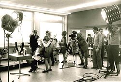 Ein Filmset, aufgebaut im bbz Arnsberg. Zu sehen sind Scheinwerfer, Mitarbeiter und ein Kameramann, der eine Friseurin filmt.