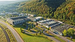 Luftaufnahme des bbz Arnsberg. Mehrere große Hallen und weitere Gebäude am Rand von bewaldeten Hügeln. 