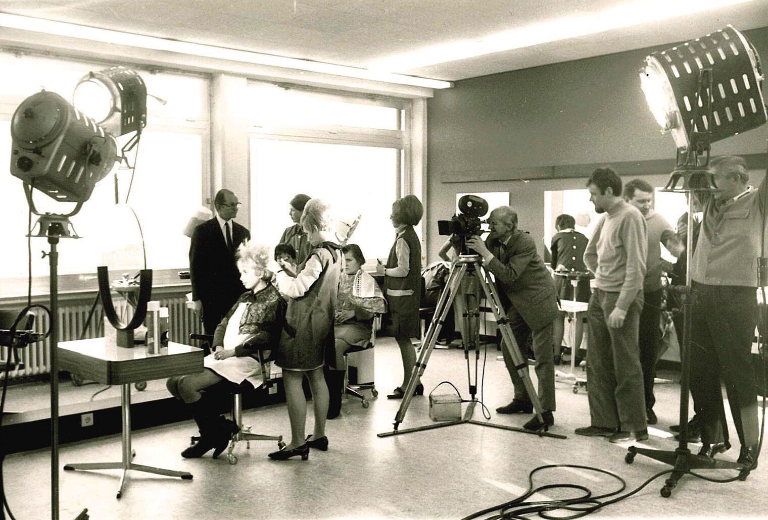 Ein Filmset, aufgebaut im bbz Arnsberg. Zu sehen sind Scheinwerfer, Mitarbeiter und ein Kameramann, der eine Friseurin filmt.