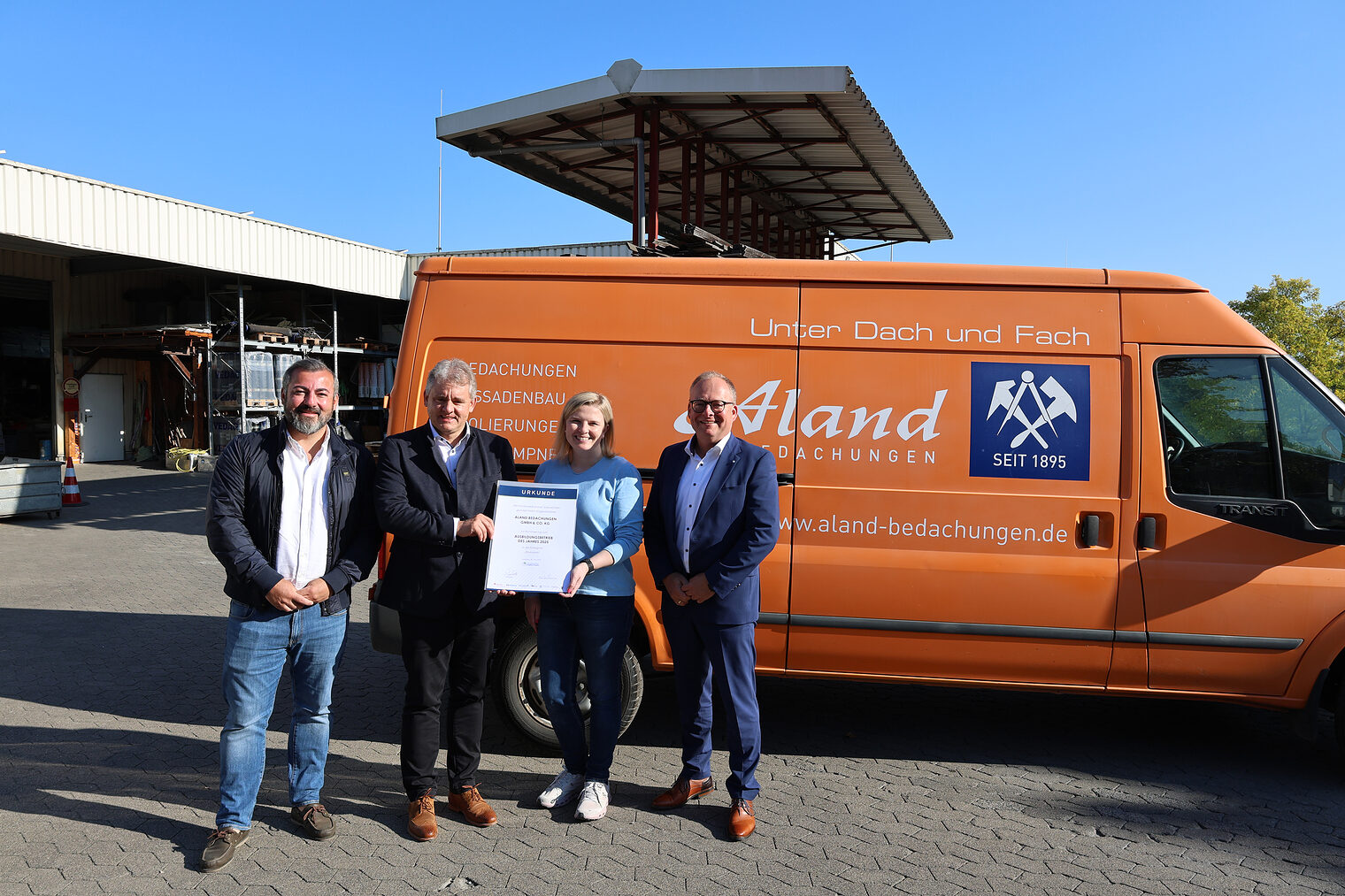 Gruppenfoto mit Vertretern der Handwerkskammer, Signal Iduna und von Aland Bedachungen. Im Hintergrund ist das Firmengelände.