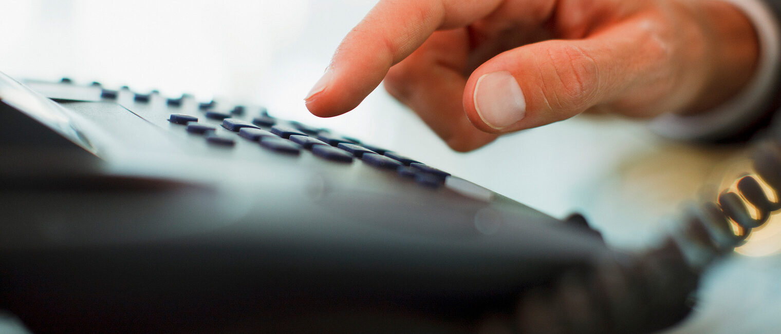 Jemand wählt eine Nummer auf einem schwarzen Festnetztelefon.