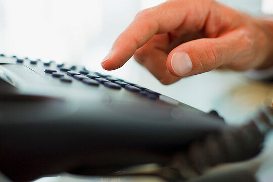 Jemand wählt eine Nummer auf einem schwarzen Festnetztelefon.