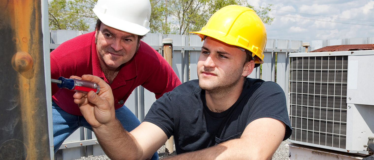 Air conditioning repair apprentice fixes an industrial compressor unit as his supervisor watches. Schlagwort(e): Alternating Current