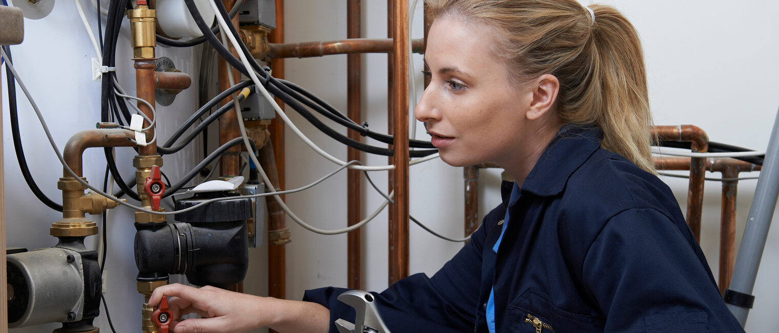 Eine Handwerkerin repariert eine Heizungsanlage in einem Keller.