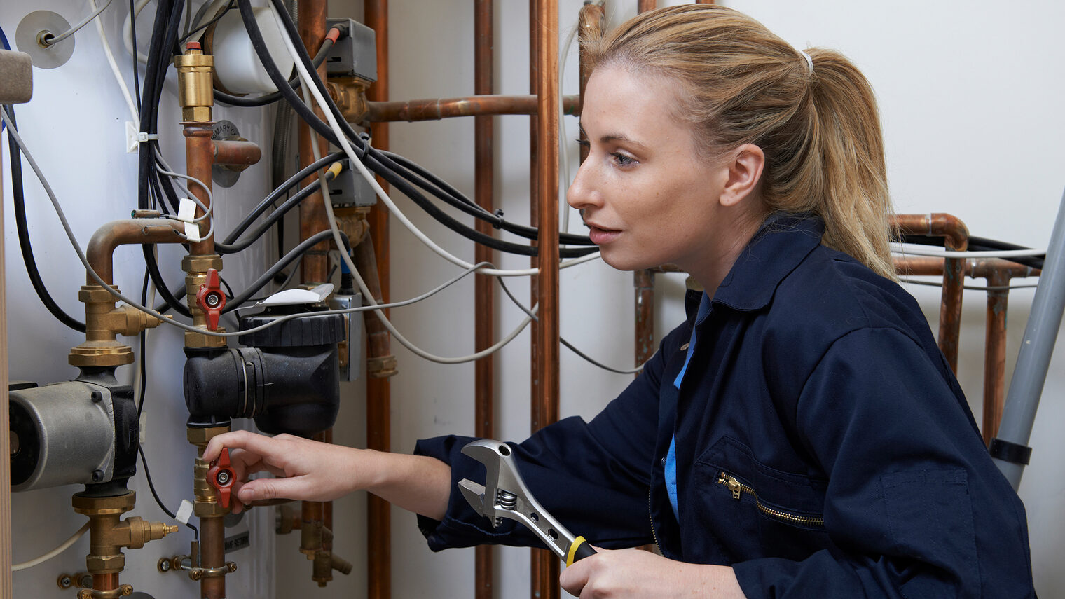 Frauen. Handwerk. Südwestfalen. Eine Handwerkerin repariert eine Heizungsanlage in einem Keller.