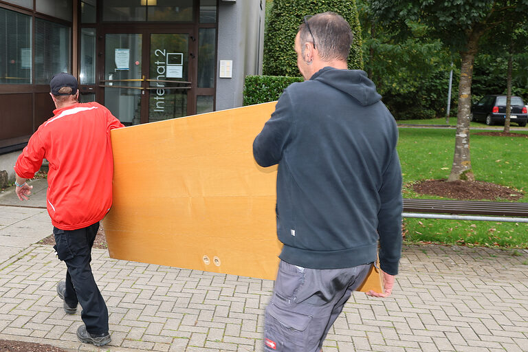 Gregor Hesse aus dem Josefsheim Bigge und Stefan Ochs, Hausmeister bei der Handwerkskammer Südwestfalen, tragen eine Tür.