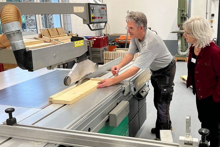 Verena Kurth mit einer Beschäftigten des Josefsheim Bigge an einer großen Holzschneidemaschine in einer Werkstatt.