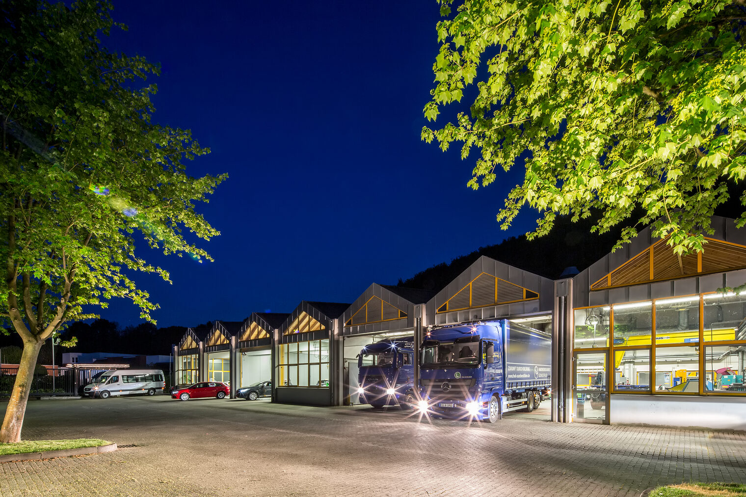 Foto einer Halle des Fachbereichs Kraft- und Nutzfahrzeugtechnik am bbz Arnsberg bei Nacht. Zwei Lkw stehen im Halleneingang.
