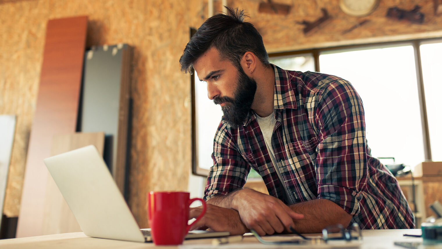 Ein Tischler arbeitet an einem Laptop in seiner Werkstatt.