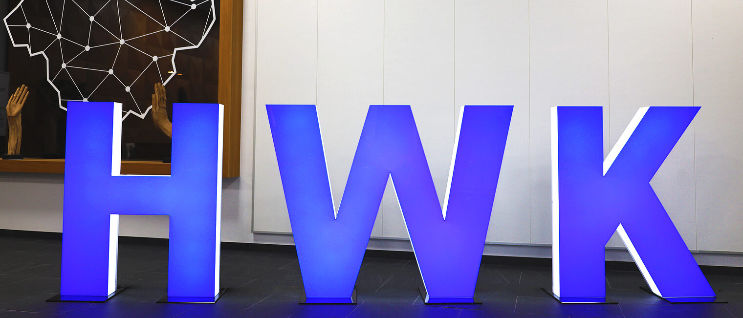 Skulpturen der Buchstaben HWK (Abkürzung für Handwerkskammer) stehen blau leuchtend im Foyer der Handwerkskammer Südwestfalen