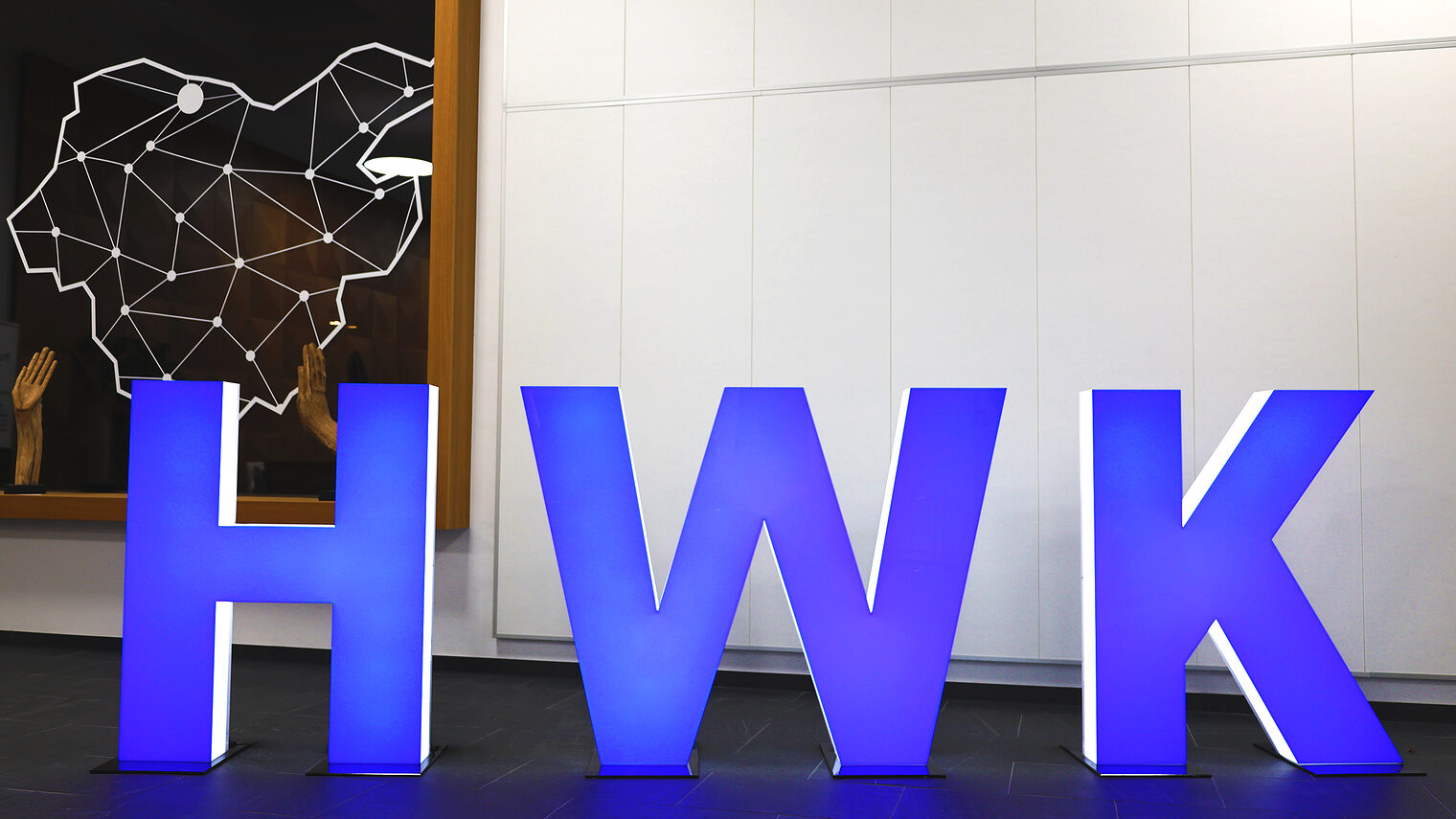 Skulpturen der Buchstaben HWK (Abkürzung für Handwerkskammer) stehen blau leuchtend im Foyer der Handwerkskammer Südwestfalen