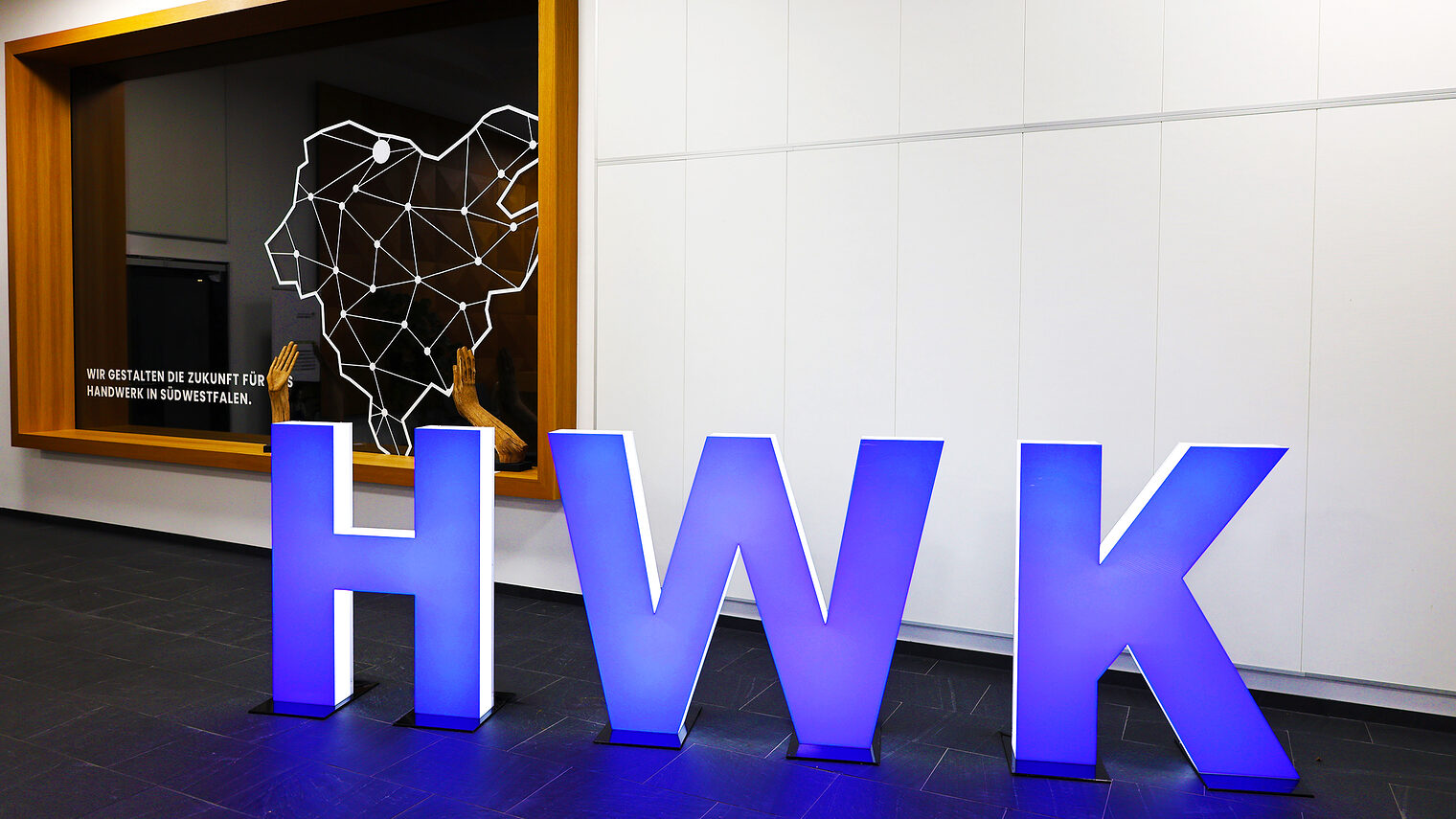 Skulpturen der Buchstaben HWK (Abkürzung für Handwerkskammer) stehen blau leuchtend im Foyer der Handwerkskammer Südwestfalen