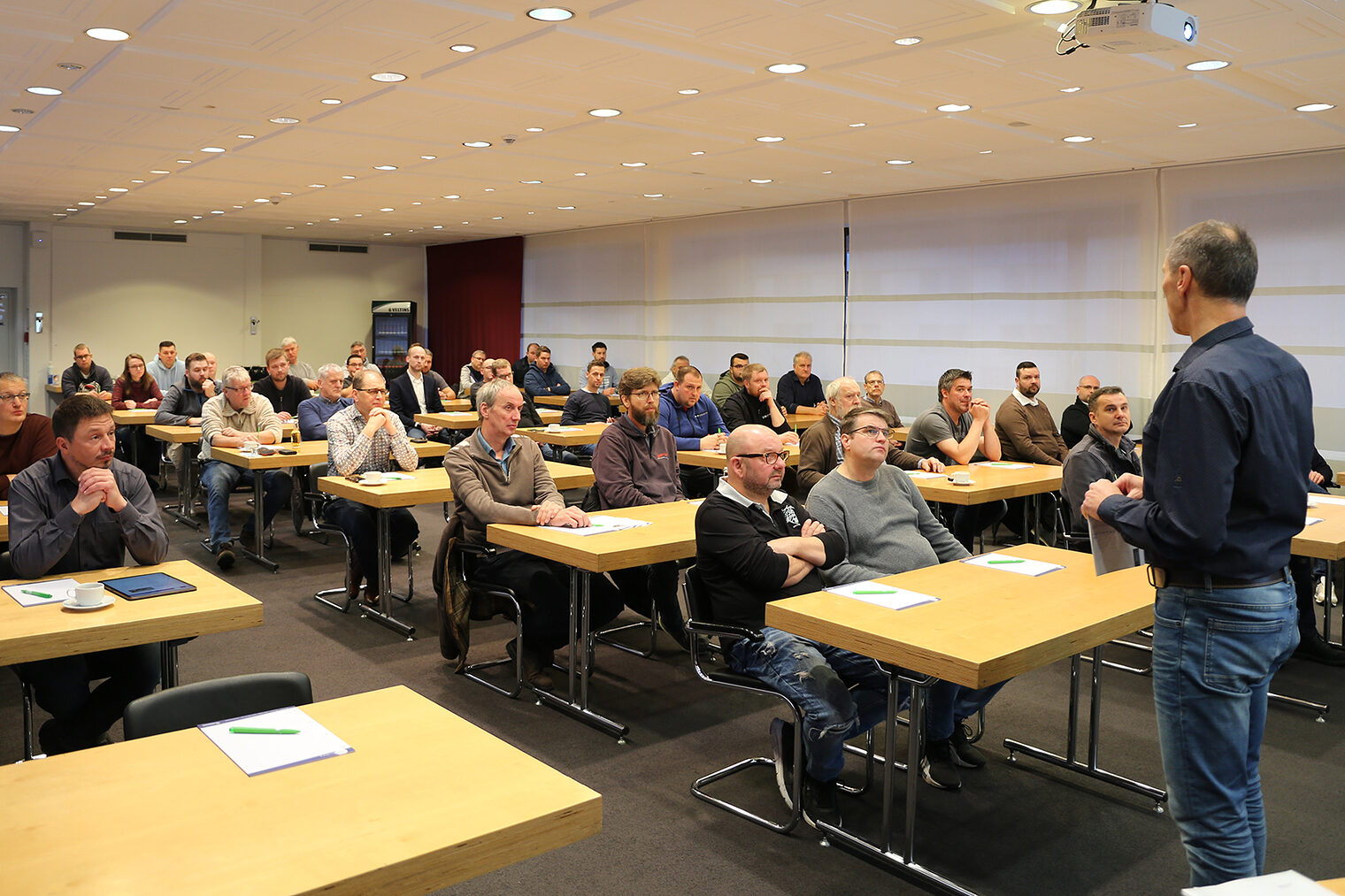 Voller Kursraum am bbz Arnsberg. Ein Dozent steht vorne und trägt vor, die Kursteilnehmer sitzen an den Tischen und hören zu.