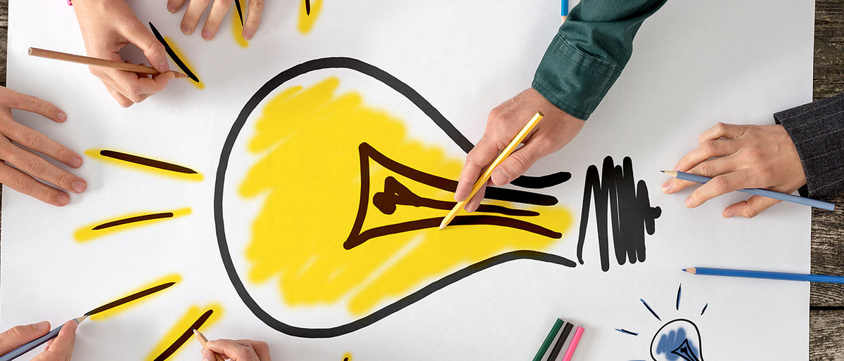 Top view of six people, men and women, drawing bright yellow light bulb on a large sheet of paper or placard. Conceptual of teamwork, research, education and innovation. Schlagwort(e): Women, Men, Group Of People, Brainstorming, Meeting, Cooperation, Teamwork, Partnership, Togetherness, Creativity, Yellow, Human Hand