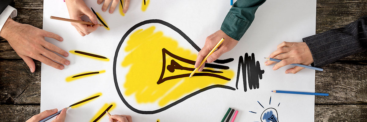 Top view of six people, men and women, drawing bright yellow light bulb on a large sheet of paper or placard. Conceptual of teamwork, research, education and innovation. Schlagwort(e): Women, Men, Group Of People, Brainstorming, Meeting, Cooperation, Teamwork, Partnership, Togetherness, Creativity, Yellow, Human Hand