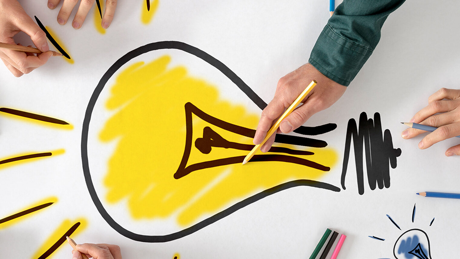 Top view of six people, men and women, drawing bright yellow light bulb on a large sheet of paper or placard. Conceptual of teamwork, research, education and innovation. Schlagwort(e): Women, Men, Group Of People, Brainstorming, Meeting, Cooperation, Teamwork, Partnership, Togetherness, Creativity, Yellow, Human Hand