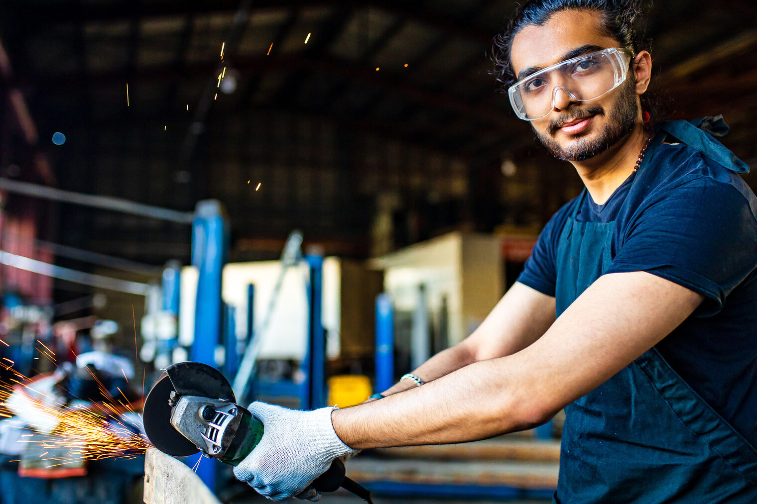 Ein Handwerker mit Schutzbrille und Schutzhandschuhen arbeitet in einer Werkstatt.