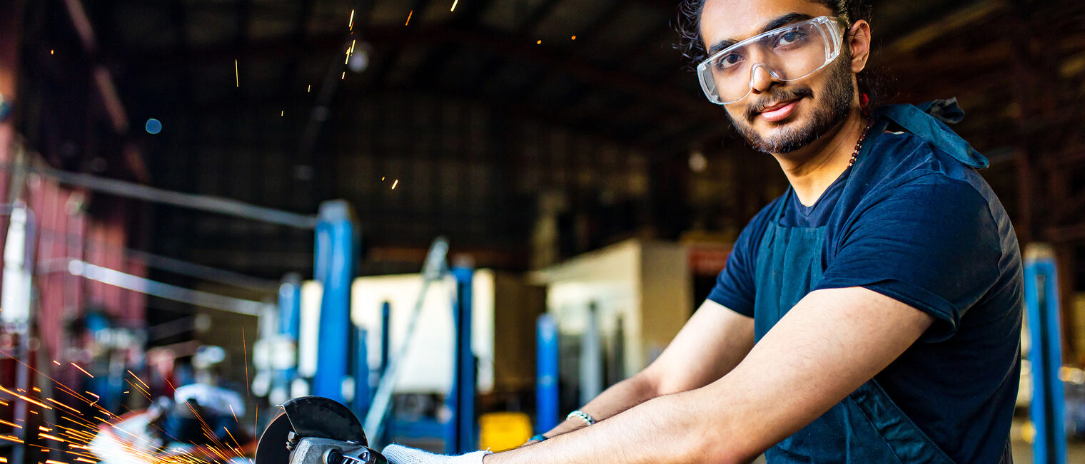 Ein Handwerker mit Schutzbrille und Schutzhandschuhen arbeitet in einer Werkstatt.