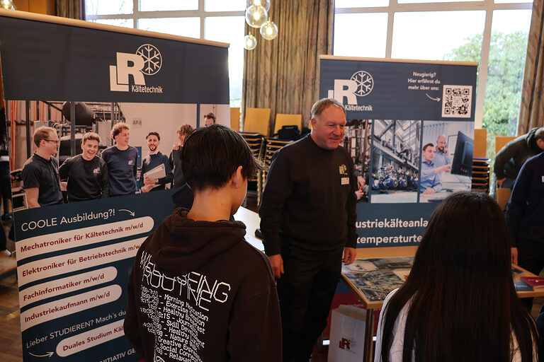 Zwei Mitarbeiter der Firma L&R Kältetechnik stellen ihren Betrieb einer Gruppe von Schülern vor.