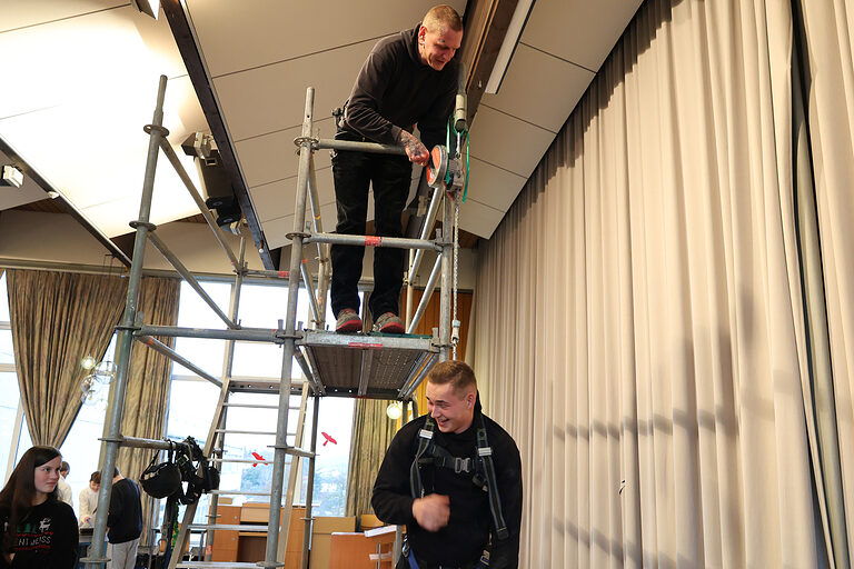 Zwei Mitarbeiter des Gerüstbauers Steinberg Gerüstbau führen ein Höhenrettungsgerät an einem Baugerüst vor.