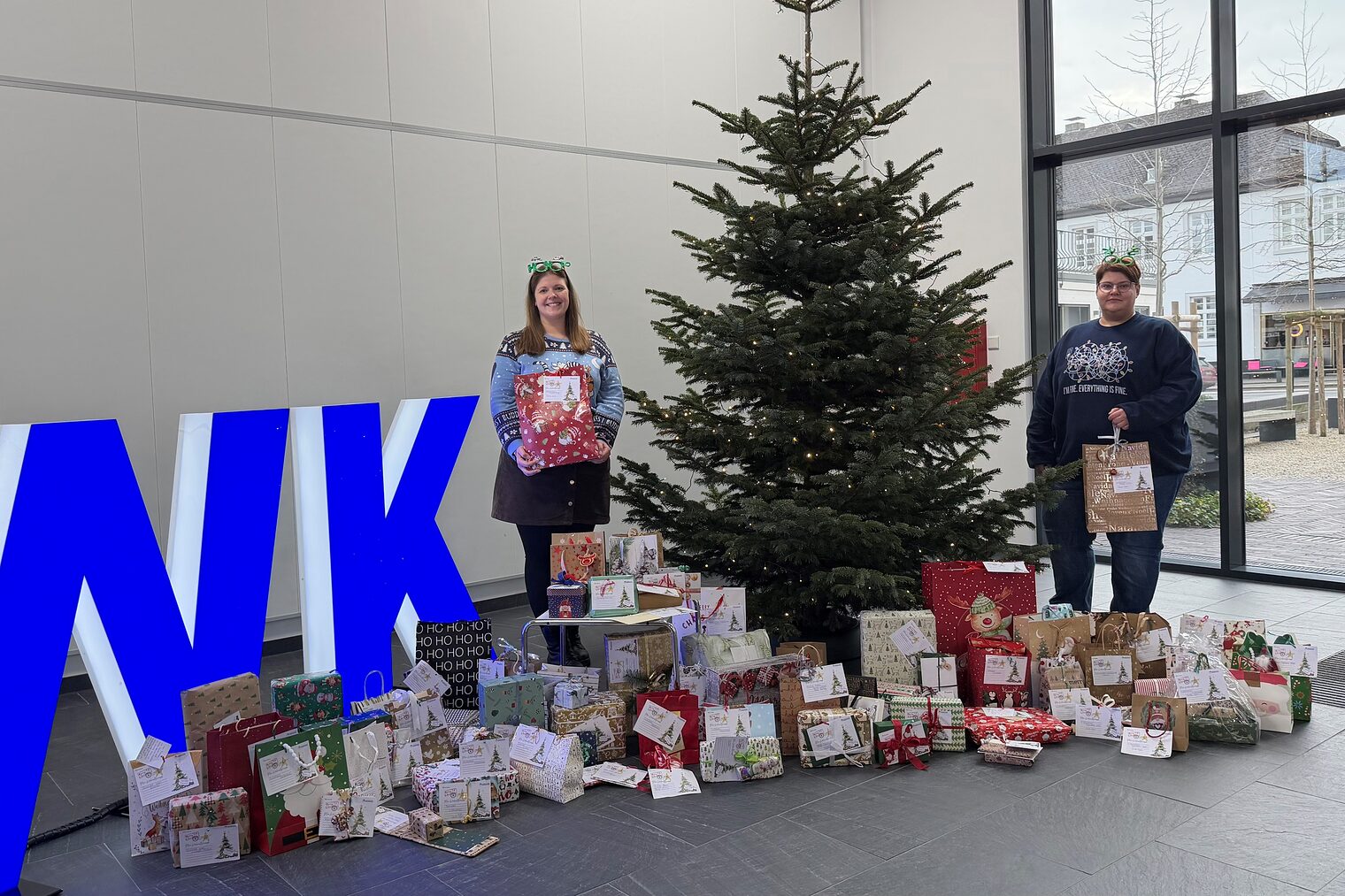 Zwei Handwerkskammer-Mitarbeiterinnen neben einem Weihnachtsbaum, um den herum verpackte Geschenke liegen.