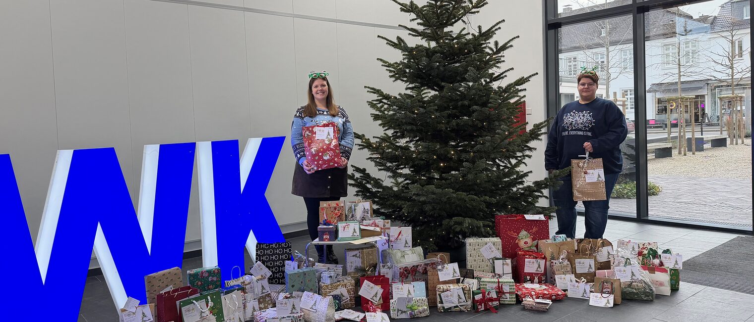 Zwei Handwerkskammer-Mitarbeiterinnen neben einem Weihnachtsbaum, um den herum verpackte Geschenke liegen.