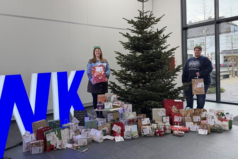 Zwei Handwerkskammer-Mitarbeiterinnen neben einem Weihnachtsbaum, um den herum verpackte Geschenke liegen.