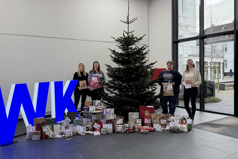 Vier Mitarbeiterinnen stehen mit Geschenken neben dem Weihnachtsbaum im Foyer der Handwerkskammer Südwestfalen.