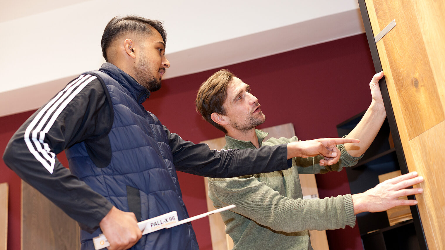 Ein Auszubildender im Gewerk Parkettleger lässt sich etwas von seinem Ausbilder zeigen.