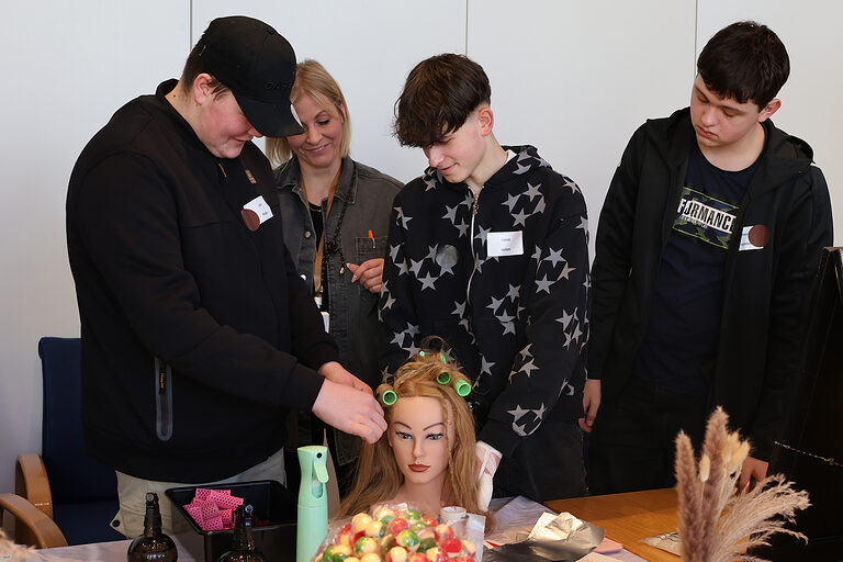 Drei Schüler wickeln Locken an einem Übungskopf der Friseur-Innung Westfalen-Süd.