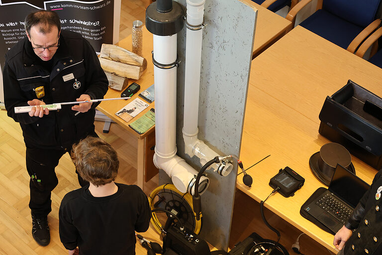 Ein Schornsteinfeger erklärt einem Schüler, wie er eine Leitung ausmessen kann.