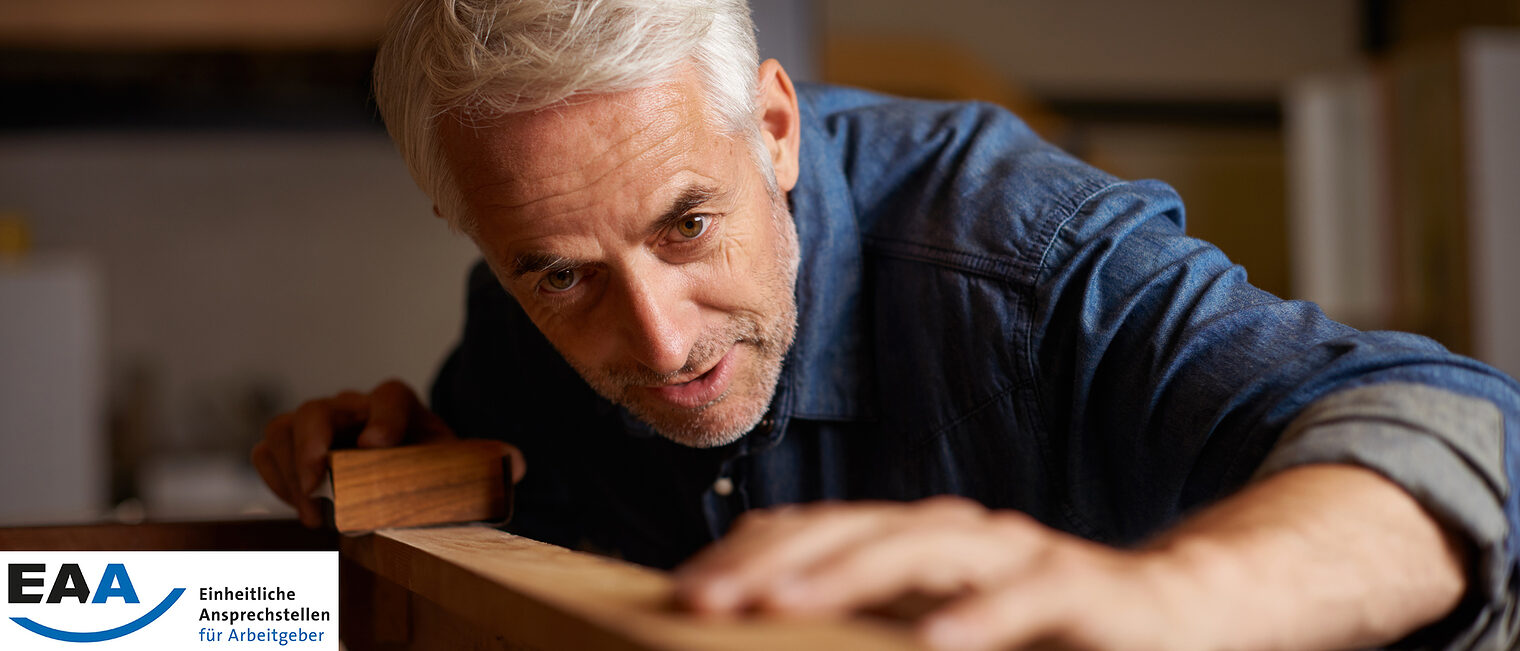 Ein Mann mit grauen Haaren arbeitet mit Holz in einer Tischlerei.