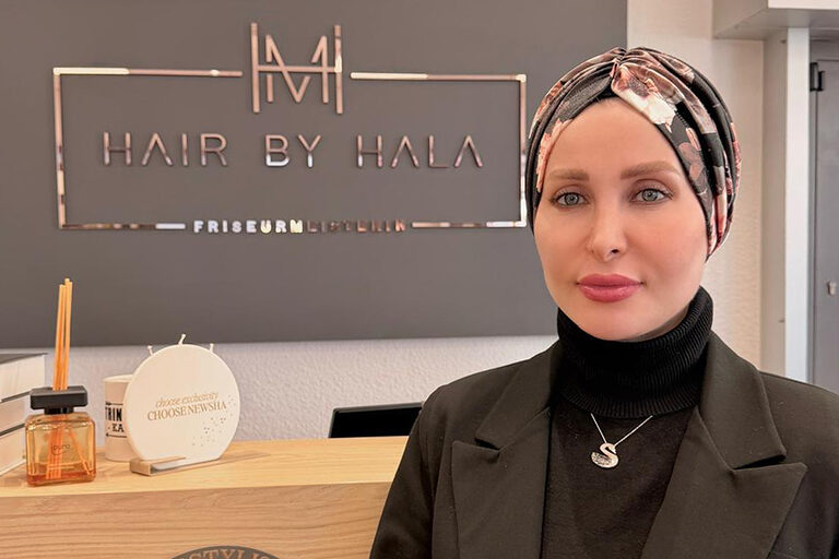 Eine Frau in dunkler Kleidung steht vor dem Empfangstresen in einem Friseursalon.