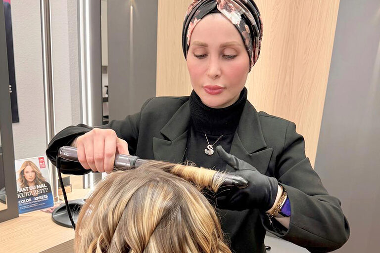 Eine Friseurmeisterin frisiert mit einem Lockenstab die Haare einer Kundin.