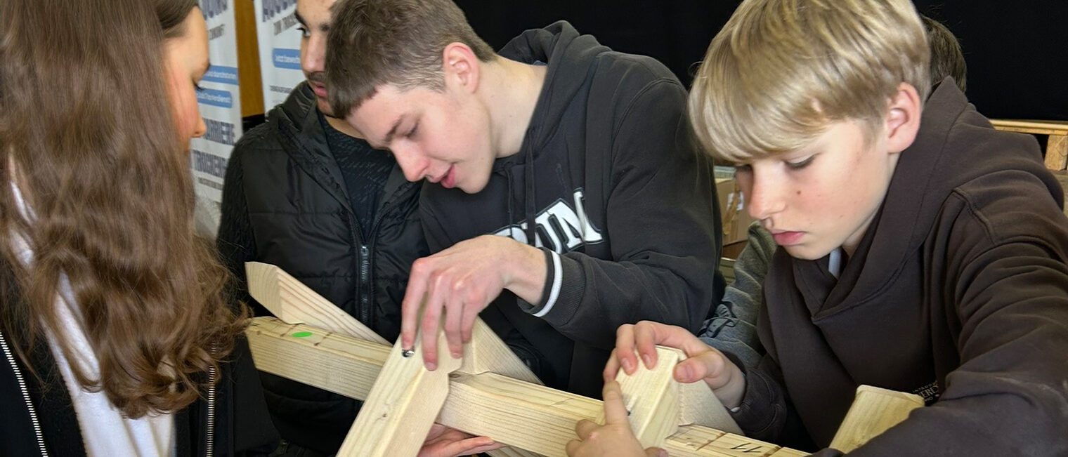 Zwei Jungs und ein Mädchen arbeiten mit Holzbalken.