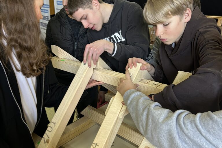 Zwei Jungs und ein Mädchen arbeiten mit Holzbalken.