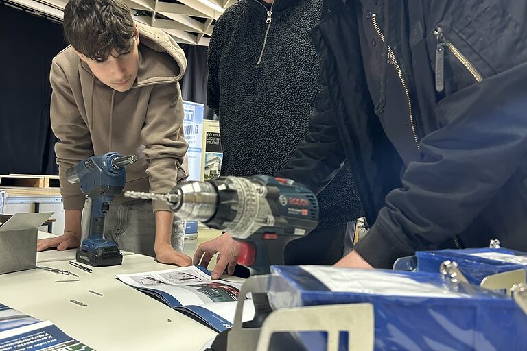 Drei Schüler schauen in eine Anleitung und diskutieren darüber.