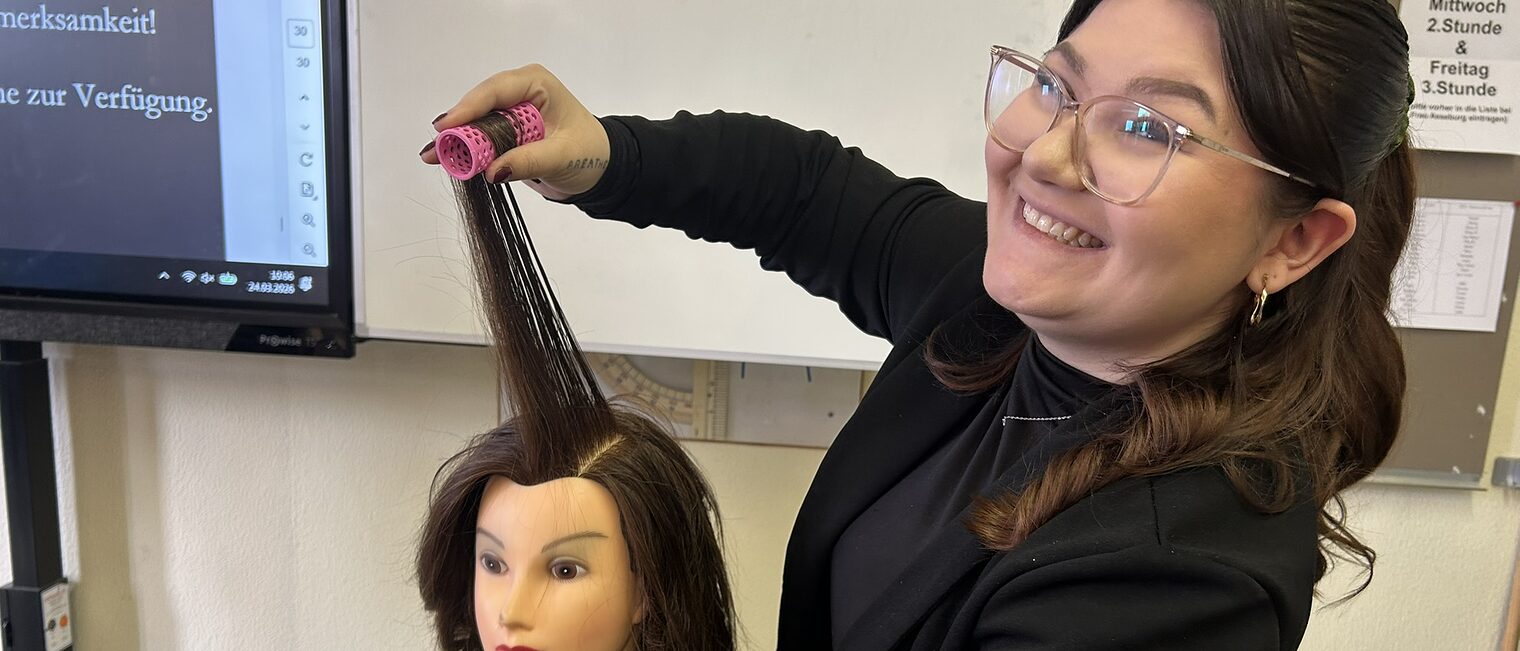 Eine Friseurin zeigt an einem Übungskopf, wie sie Locken wickelt.