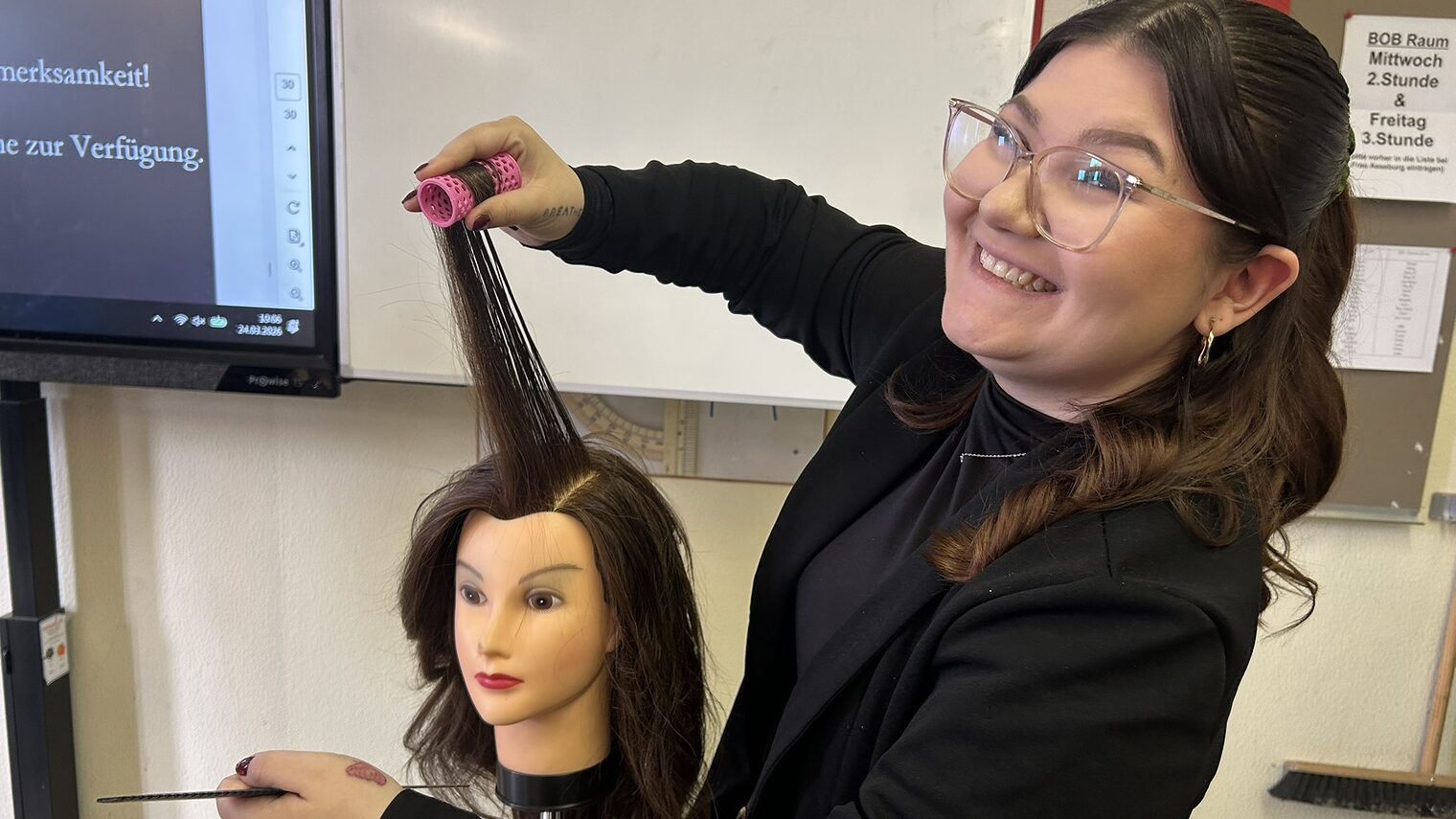 Eine Friseurin zeigt an einem Übungskopf, wie sie Locken wickelt.