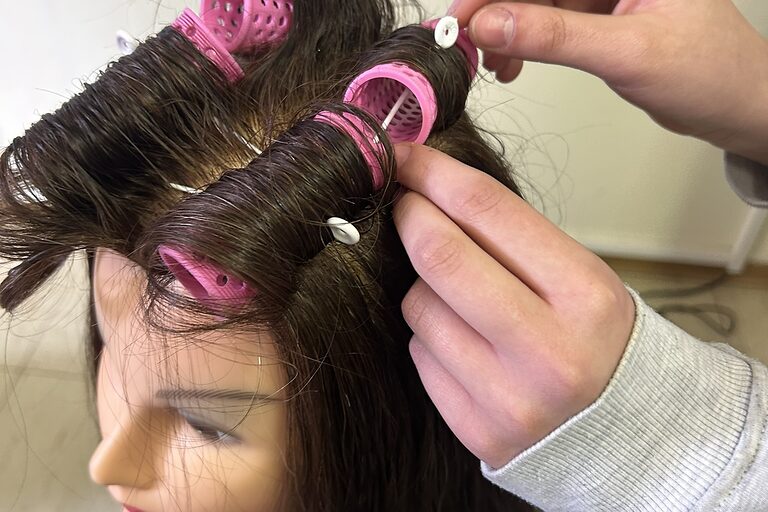 Nahaufnahme, wie jemand Locken an einem Übungskopf wickelt.