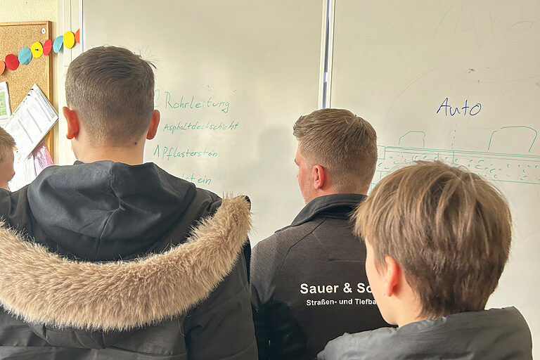 Drei junge Männer an einem Stand eines Handwerkbetriebs bei einem Handwerkstag in einem Schulgebäude.